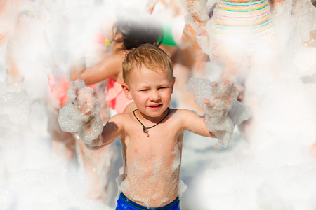 Foam Party on the beach. Baby boy having fun and dancing in a foam.の写真素材