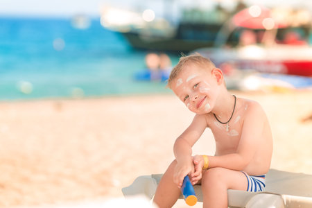 Cute little boy with sunscreen on holding the bottle of sunscreen lotion on the beachの写真素材
