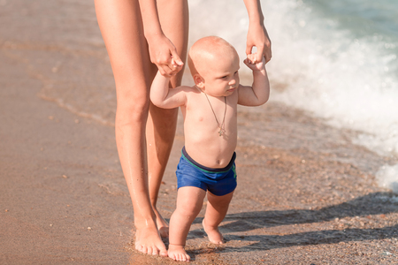 Cute little baby walking along the seaside with his sister. Baby's first steps on the beach.の写真素材