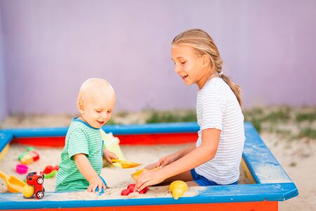 Cute baby boy playing with his sister with toys in the sandbox outdoorの写真素材