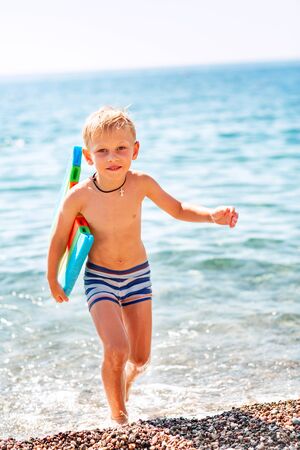 Happy little boy playing with swimming kickboard in the waves at the seasideの写真素材