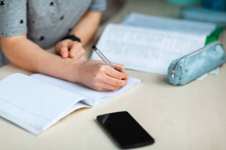 Close up of young school girl working at home in her room with class notes checking mobile phone and studying. Distance education and learning concept during quarantineの写真素材