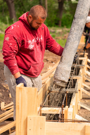Construction worker laying cement or concrete into the foundation formwork with automatic pump....
