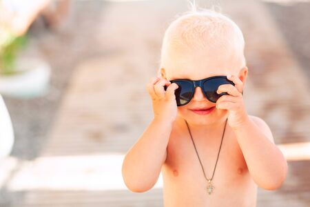 Cute baby boy posing in big sunglasses on the beachの写真素材