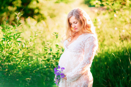 Beautiful young pregnant woman relaxing in nature on a beautiful sunny day with field in the background.の写真素材