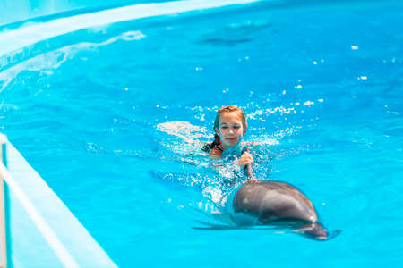 Happy little girl swimming with dolphins in Dolphinarium. Swimming, bathing and communication with dolphins.の写真素材