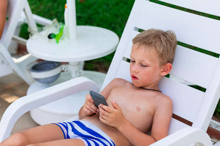 Boy playing games on the telephone. Gadget dependency disorder problem for kids during holiday vacation at the seaside conceptの写真素材