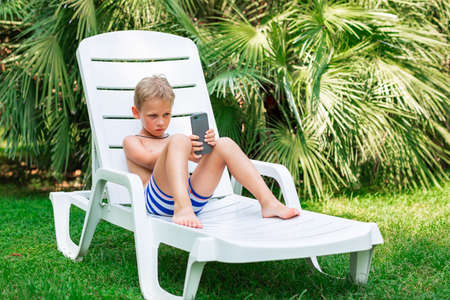 Boy playing games on the telephone. Gadget dependency disorder problem for kids during holiday vacation at the seaside conceptの写真素材