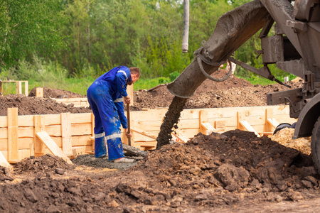 Construction worker laying cement or concrete into the foundation formwork. Building house...