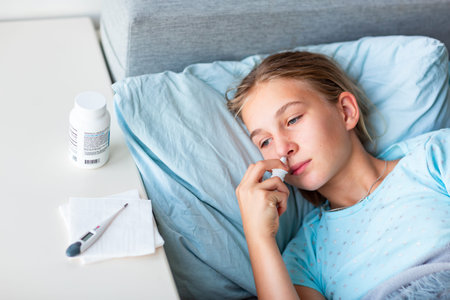Sick teenage little girl with high fever and headache laying in bed spraying medicine into her nose....