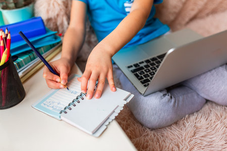 Little young school boy working at home with a laptop and class notes studying in a virtual class....