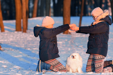 Beautiful teenage girls having fun with spitz dog in the park in winterの写真素材