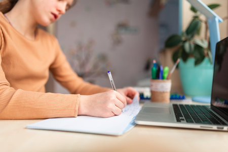 Beautiful schoolgirl studying at home doing school homework. Hand's close-up. Training books and...