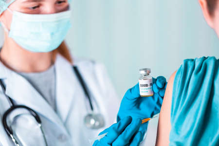 Woman doctor or nurse in uniform and gloves wearing face mask protective in lab, making an injecion holding vaccine bottle with COVID-19 Coronovirus vaccine labelの写真素材