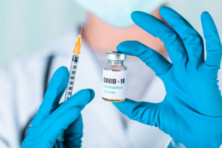 Woman doctor or nurse in uniform and gloves wearing face mask protective in lab, holding medicine vial vaccine bottle with COVID-19 Coronavirus vaccine labelの写真素材