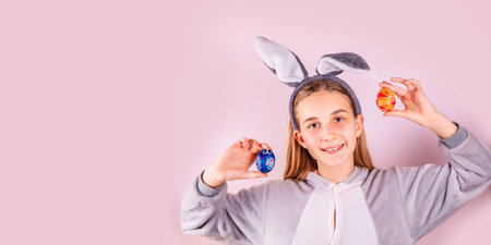 Girl in rabbit bunny ears on head with colored eggs on pink background. Cheerful smiling happy...