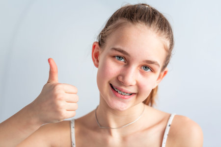 Teenage girl smiling in orthodontic brackets showing thumb up. Girl with braces on teeth....