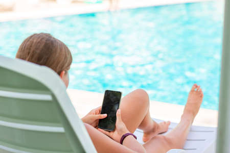 Teenage girl playing games and searching web on the telephone at the pool on vacation. Gadget dependency disorder problem for kids during holiday vacation at the seaside conceptの写真素材
