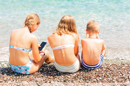 Children playing games and searching web on the telephones at the beach. Gadget dependency disorder problem for kids during holiday vacation at the seaside conceptの写真素材