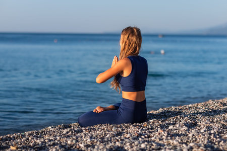 Young girl sitting in Lotus pose on the beach at sunset. Beautiful girl practicing Yoga during summer Vacation Meditation Seaside Sea Ocean Holiday Travelの写真素材