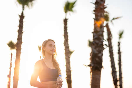 Young girl exercising on seafront line at sunset sunrise. Beautiful girl drinking water while jogging on sea promenade during summer Vacation Meditation Seaside Sea Ocean Holiday Travelの写真素材
