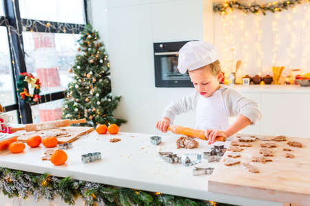 Cute little boy making gingerbread, cutting cookies of gingerbread dough. Christmas bakery. Festive food, cooking process, family culinary, Christmas and New Year traditions conceptの写真素材