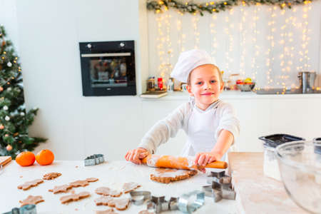 Cute little boy making gingerbread, cutting cookies of gingerbread dough. Christmas bakery. Festive food, cooking process, family culinary, Christmas and New Year traditions conceptの写真素材