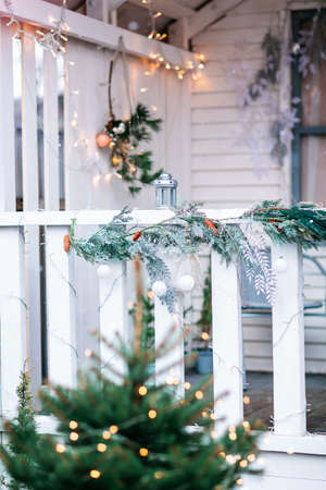 White house with porch decorated with Christmas decorations and Christmas tree. Spruce garlands around the door. Beautiful winter terrace of the house with garlands and lights.の写真素材