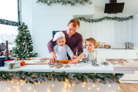 Father with two kids cooking making gingerbread, cutting cookies of gingerbread dough, having fun. Festive food, cooking process, family culinary, Christmas and New Year traditions concept. Christmas bakery.の写真素材