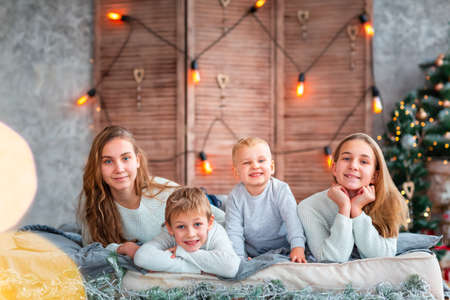 Happy kids siblings having fun on the bed near the Christmas tree on Christmas morning. Christmas family morning, christmas mood conceptの写真素材