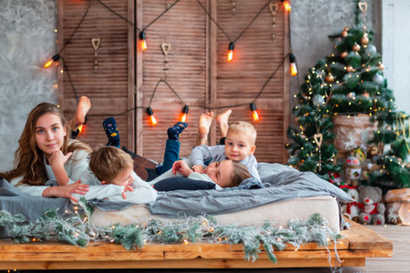 Happy kids siblings having fun on the bed near the Christmas tree on Christmas morning. Christmas family morning, christmas mood conceptの写真素材