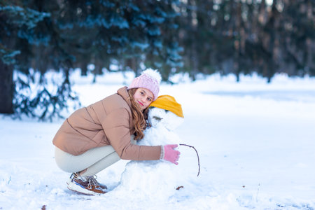 Cute little teenage girl having fun playing making snowman in the snowy winter forest. Snow games. Winter vacation.の写真素材