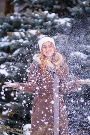 Winter girl throwing snowball at camera smiling happy having fun outdoors on snowing winter day playing in snow. Cute playful redhead ginger young woman outdoor enjoying first snow.の写真素材