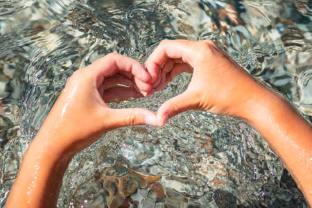 Hands forming heart shape on the sea waves background. Holiday, rest, vacation at the seaside conceptの写真素材