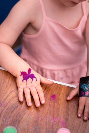 Little girl getting glitter tattoo at birthday party. Shimmering sparkling tattoo on a child's hand. Body artの写真素材