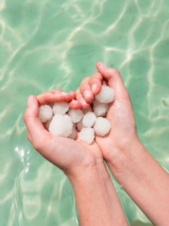 Hands holding sea salt crystals heart-saped on sea water background. Dead sea salt spa minerals cosmetic conceptの写真素材