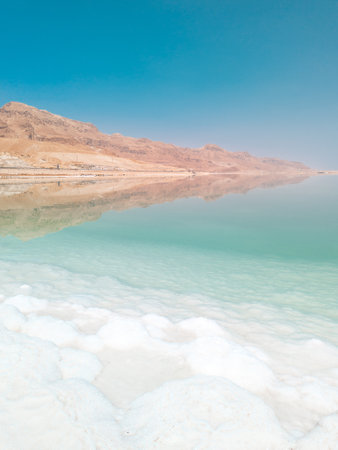 Landscape view on Dead Sea salt crystals formations, clear cyan green calm water and mountains at Ein Bokek beach, Israelの写真素材