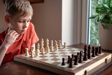 Young white child playing a game of chess on large chess board. Chess board on table in front of school boy thinking of next move, tournamentの写真素材