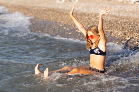 Teenage girl in pink sunglasses having fun on the beach in the sea, playing with waves and splashes. Fun on summer hloiday concept.の写真素材