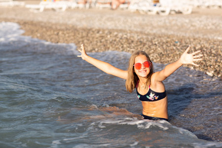 Teenage girl in pink sunglasses having fun on the beach in the sea, playing with waves and splashes. Fun on summer hloiday concept.の写真素材