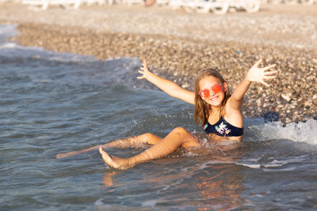 Teenage girl in pink sunglasses having fun on the beach in the sea, playing with waves and splashes. Fun on summer hloiday concept.の写真素材