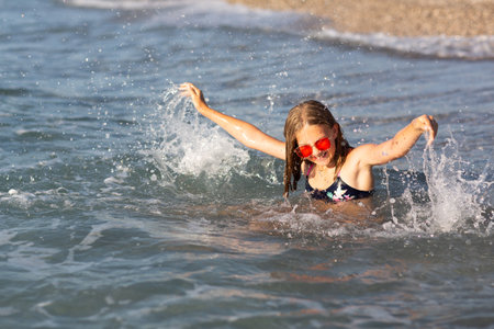 Teenage girl in pink sunglasses having fun on the beach in the sea, playing with waves and splashes. Fun on summer hloiday concept.の写真素材