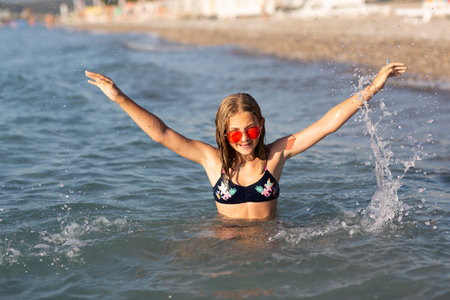 Teenage girl in pink sunglasses having fun on the beach in the sea, playing with waves and splashes. Fun on summer hloiday concept.の写真素材