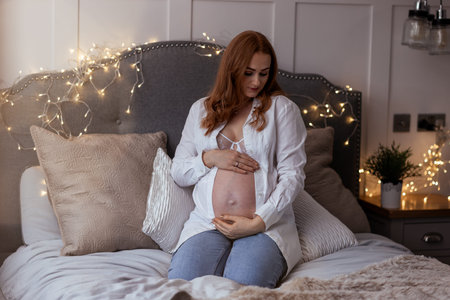 Beautiful redhead middle age pregnant woman expecting a baby sitting on the bed at home