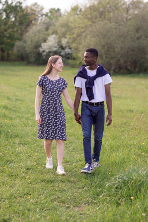 Young couple enjoying a summer day outdoors a Black man and a White woman together in a natural garden field, expressing romance, love, and diversity in a peaceful, sunny settingの写真素材