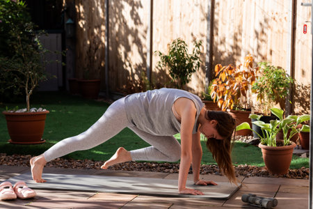 A teenage girl performing mountain climbers on a yoga mat in her backyard garden. Outdoor fitness...