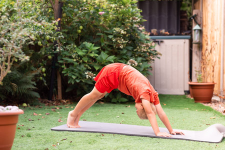 A young boy practicing yoga and fitness exercises on a mat in his backyard garden. Outdoor activity...