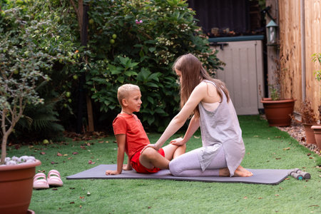 Brother and sister practicing yoga together outdoors in a sunny backyard. Teenage girl and younger boy doing fitness exercises on yoga mats, enjoying family time and a healthy lifestyle. Active children stretching and relaxing during morning workout in the garden, concept of mindfulness, balance, and wellbeing at home.の写真素材