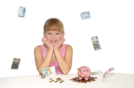 Smiling girl sitting on table with piggy bank and flying euro aroundの写真素材