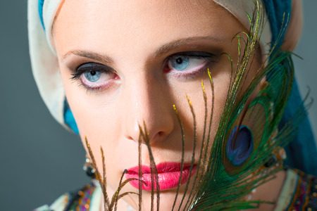 Close up portrait of beautiful  woman  with blue eyes with peacock featherの写真素材